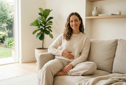 Smiling woman sitting comfortably on a sofa at home, hand resting on her abdomen, conveying relief from digestive discomfort.
