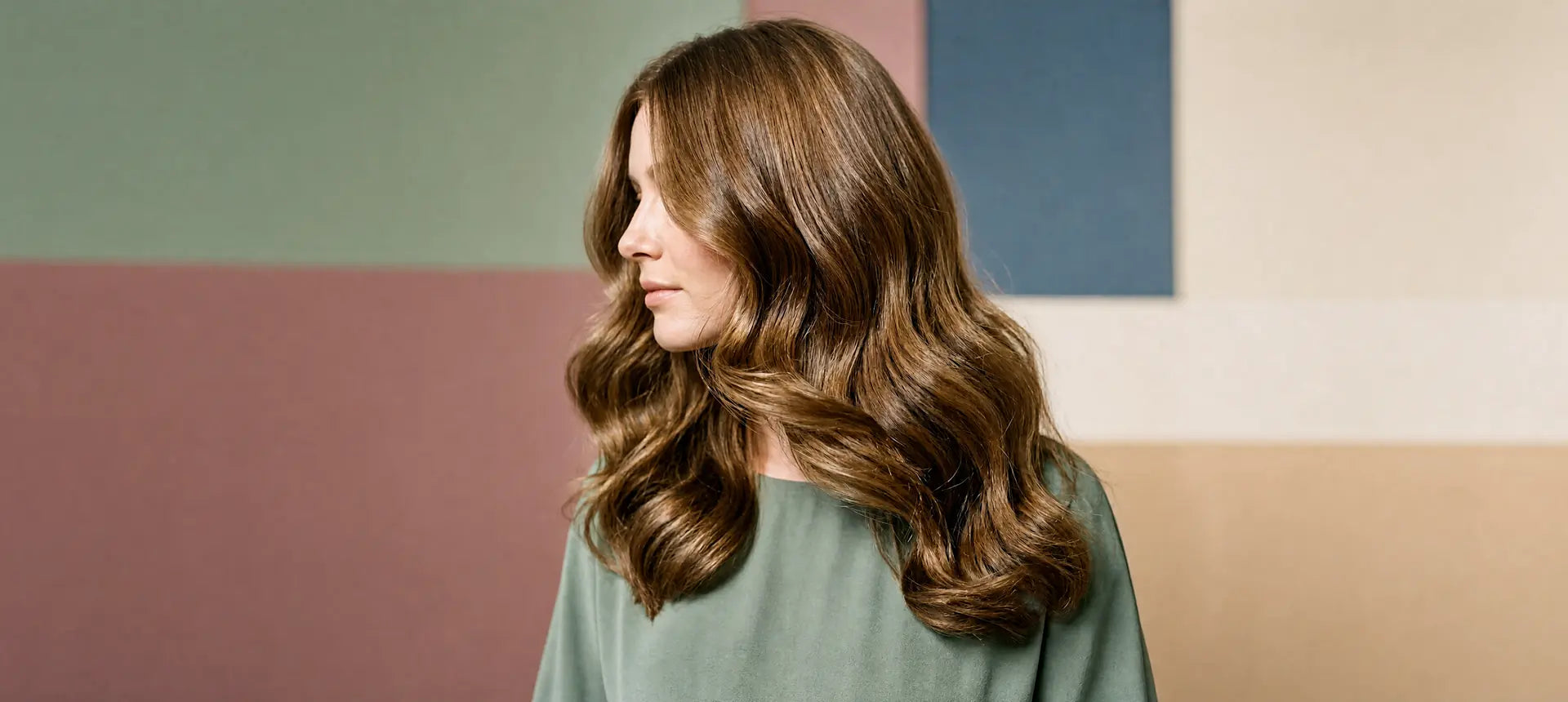 **Photo description:** A woman with long, healthy hair gently turns her head as her hair flows naturally around her face. She is smiling softly against a white background, conveying a sense of vitality, confidence, and hair radiance.