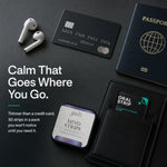 A dark promotional flat lay showing a small rectangular box of Mind Strips oral strips alongside other everyday items on a dark surface: a black credit card, white wireless earbuds, a passport, and a black wallet with an oral strip card inserted. Large text reads 'Calm That Goes Where You Go.