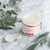An open jar of Glenari Recovery Cream sits on a white marble surface with a dollop of the white cream beside it and soft green botanical leaves around it.